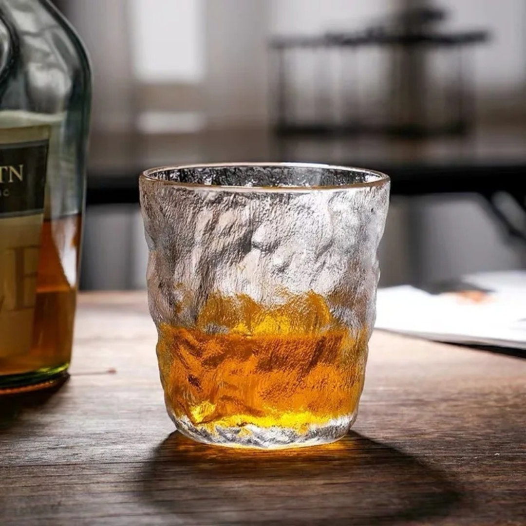 Handcrafted retro-inspired whisky glass with a unique textured surface, filled with whisky, placed on a wooden table next to a bottle.