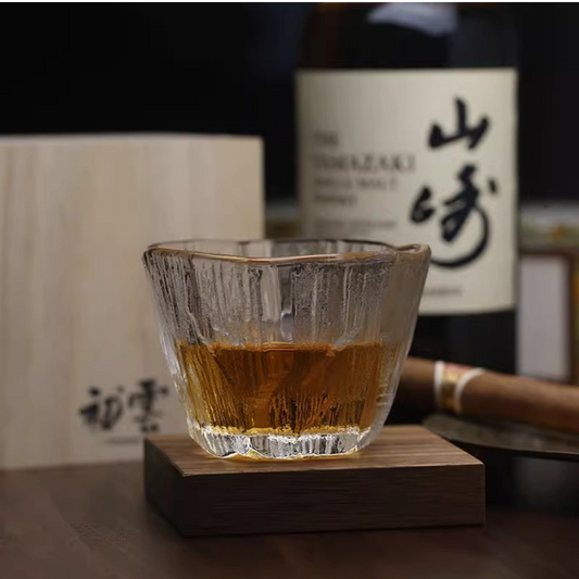 Handcrafted ice-inspired whisky glass with a unique textured surface, filled with whisky, placed on a wooden table next to a cigar and bottle.