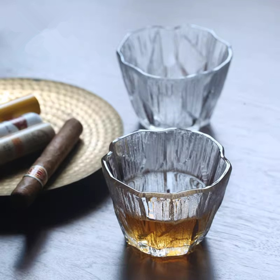 Two handcrafted ice-inspired whisky glass with a unique textured surface, one filled with whisky next to a dish of cigars.