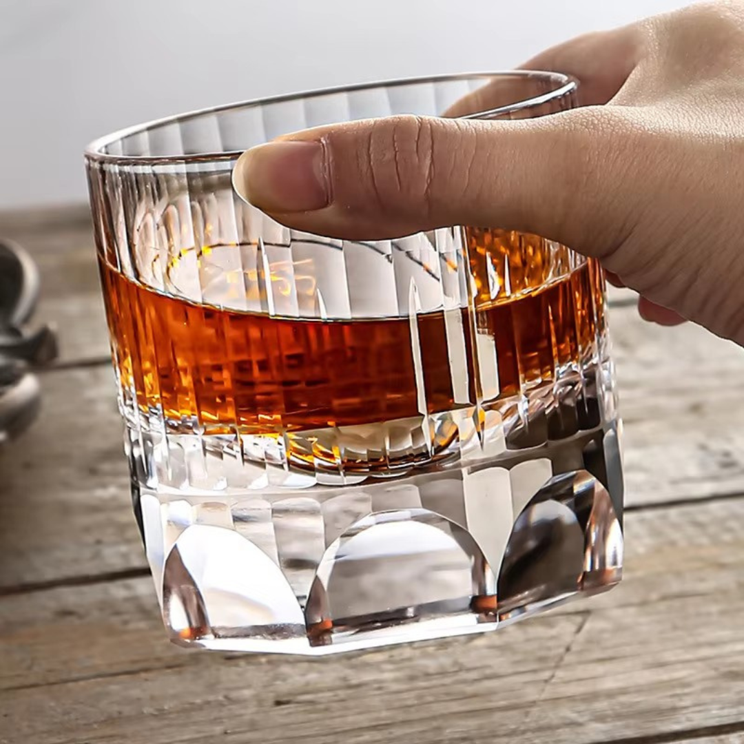 Hand holding a handcrafted K9 crystal whisky glass with a heavy bottom and intricate kiriko cut design, featuring thumbprint-inspired imprints for a comfortable grip.