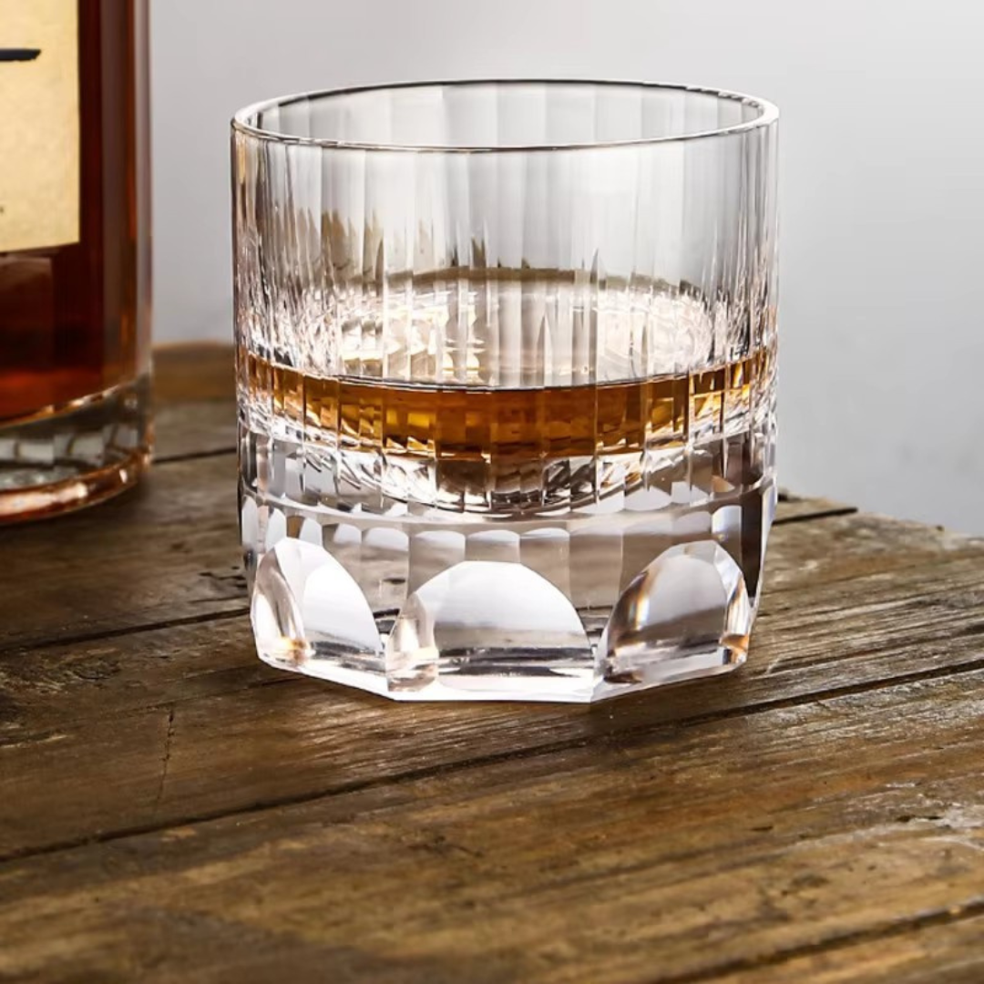 Handcrafted K9 crystal whisky glass with a heavy bottom and intricate kiriko cut design, featuring thumbprint-inspired imprints for a comfortable grip. Filled with whisky on a rustic wooden bench.