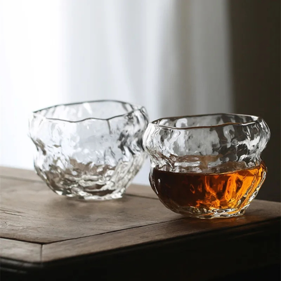 Two handcrafted whisky glass with an organic, wavy texture, filled with whisky and styled on a rustic wooden bench. Made from premium crystal for a unique and luxurious drinking experience.