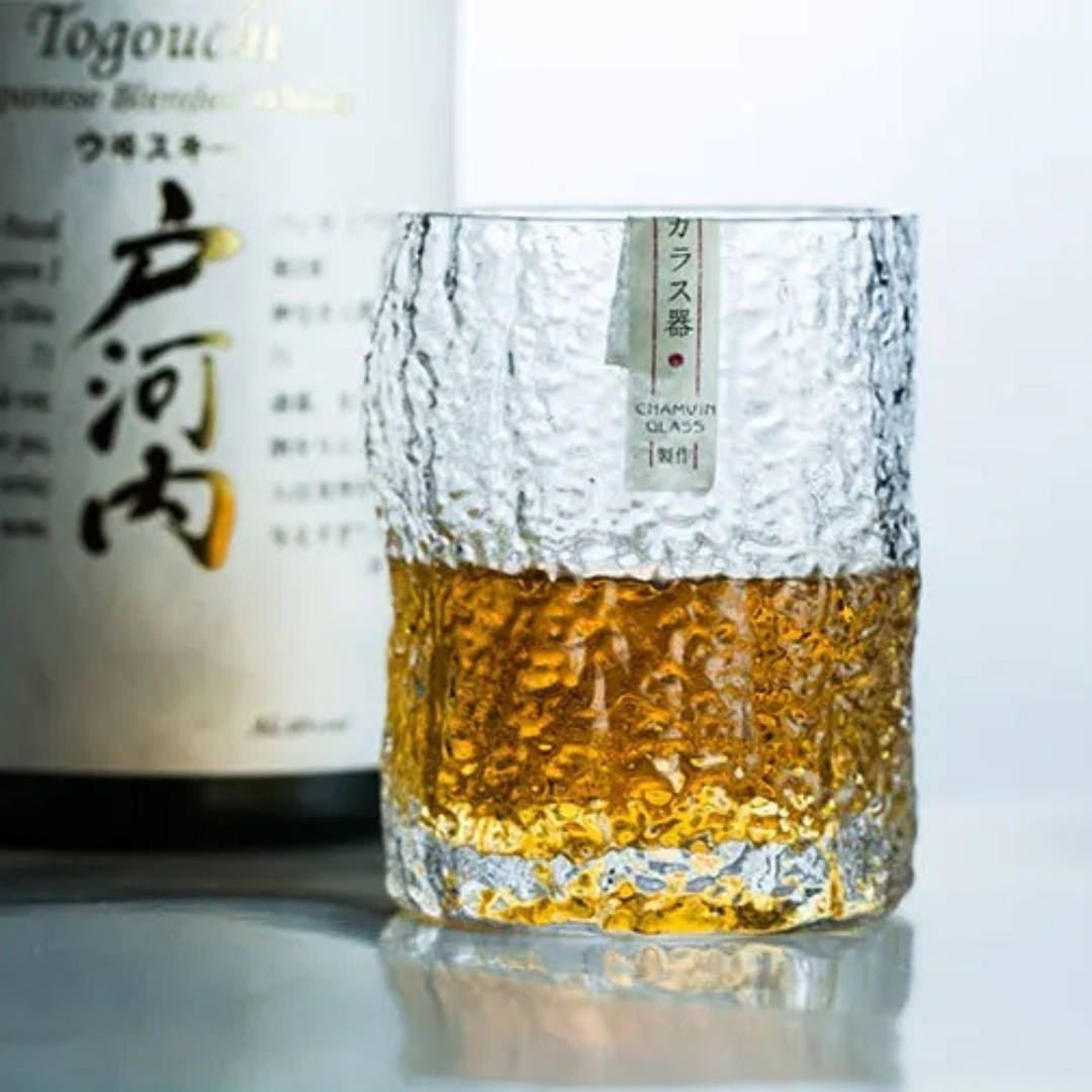 Handcrafted Edo whisky glass with a unique crumple pattern, filled with whisky, next to a bottle of whisky. The textured crystal surface catches the light, highlighting its artisanal design.